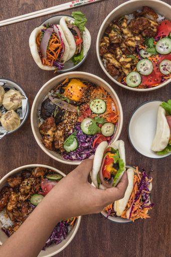 A top view shot of a table with Asian street food, poke bowl, bao, bun, chopsticks