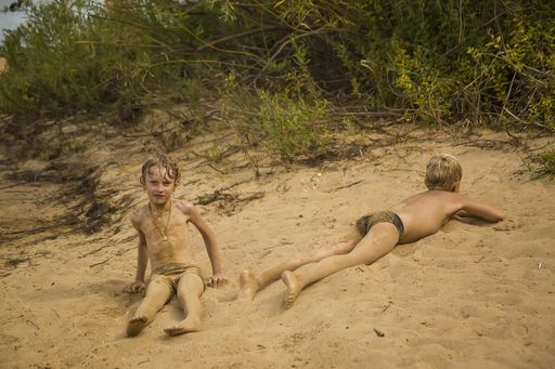 A closeup shot of a child sitting on the sand with another child lying on the sand next to him