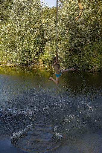 A vertical shot of a child swinging on a rope over a body of water in Moscow, Russia