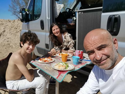 A man taking selfie of a family enjoying a meal outdoors in a motorhome