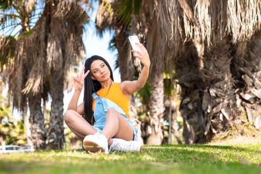 Portrait of an African American woman using the phone next to some palm trees on a sunny day on vacation