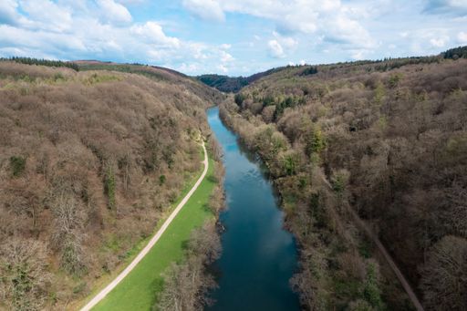 An aerial view of a blue river flowing down through forests under a bright cloudy sky