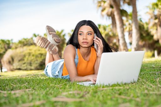 Portrait of an African American woman using the phone and the computer next to some palm trees on a sunny day