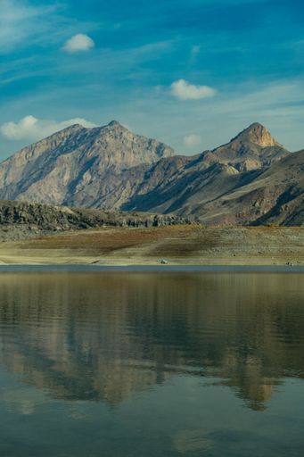A vertical shot of a small body of water reflecting the surrounding mountains under a light cloudy sky