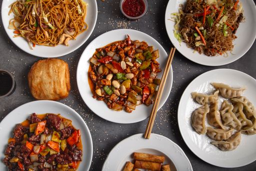 A top view of a grey table with a variety of Chiese food in white plates