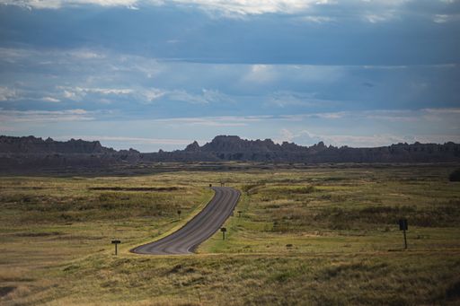 A highway amid green fields on the background of rocky mountains under the blue sky