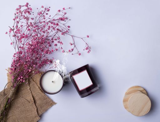 A top view of pink flowers and an aromatic candle on a plain background