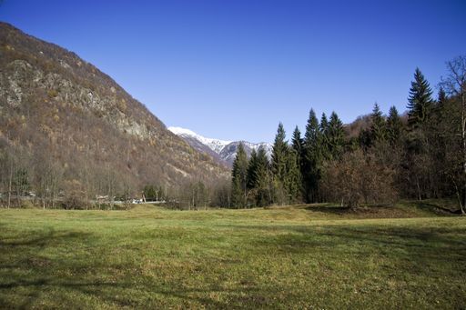A field covered in greenery surrounded by hills under the sunlight and a blue sky at daytime