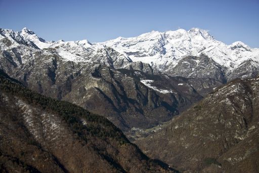 A landscape of mountains covered in trees and snow under the sunlight and a blue sky