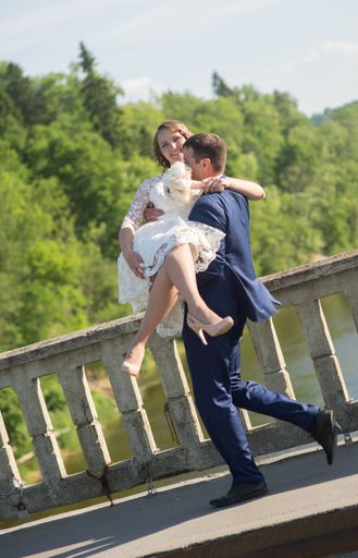 A vertical shot of the couple- the groom carrying the bride in his arms with trees in the background