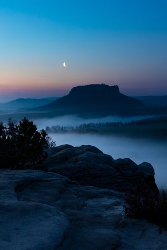 The rocky Lilienstein in Saxon Switzerland before sunrise in the delicate moonlight. The fog lies over the Elbe valley.