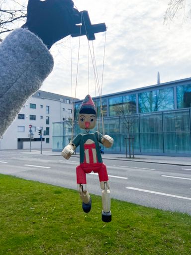 A vertical shot of a colorful wooden marionette outdoors and a hand holding it above