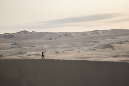 An isolated woman walking alone in the large desert under the dusk sky