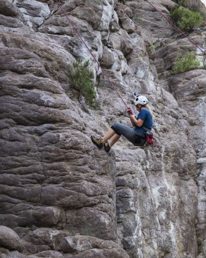 A man with a helmet and a harness trying to climb over the rocky mountain