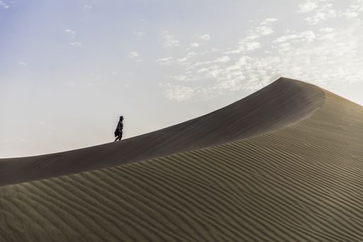 An isolated woman walking alone in the large desert under the dusk sky