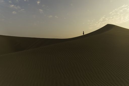 An isolated woman walking alone in the large desert under the dusk sky