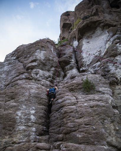 A man with a helmet and a harness trying to climb over the rocky mountain