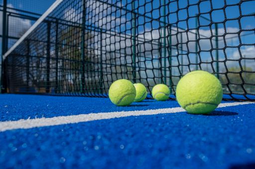 selective focus, four paddle tennis balls on a blue paddle tennis court close to the net, racket sports concept