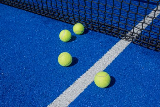 selective focus, four paddle tennis balls on a blue paddle tennis court close to the net, racket sports concept