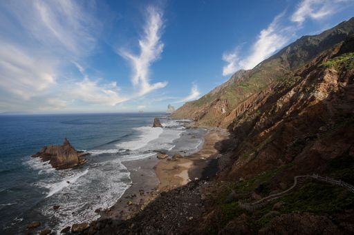 A beautiful landscape view of rock formations at the beach and mountains against blue cloudy sky on sunny day in Tenerife Island, Spain
