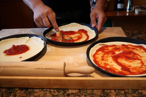 A closeup shot of a kitchen table with a person's hand preparing Italian pizza at home