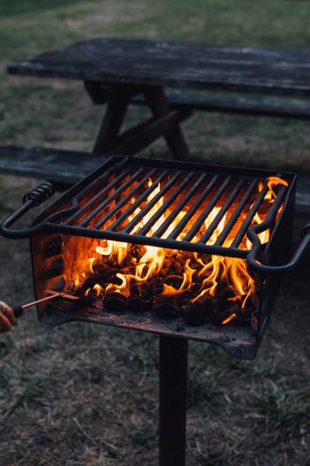 A vertical shot of a burning flame in an outdoor grill stove next to a picnic table.