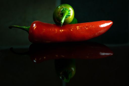 A closeup of red and green chilli pepper on the table under the lights on a blurry background