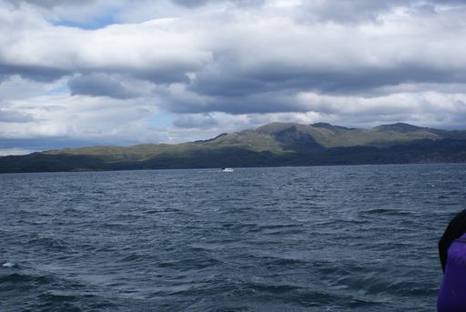 A beautiful view of sea waves with mountains background under a cloudy sky in Scotland