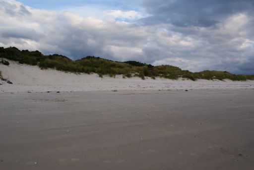 A scenic view of sandy shore and mountain landscape in Scotland under a cloudy sky