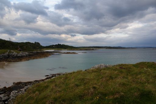 A scenic view of sandy shore and mountain landscape in Scotland under a cloudy sky