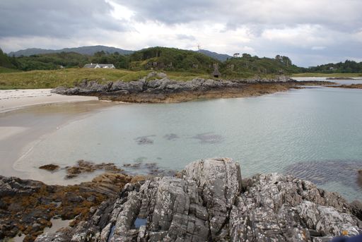 A scenic view of rocky shore and mountain landscape in Scotland under a cloudy sky
