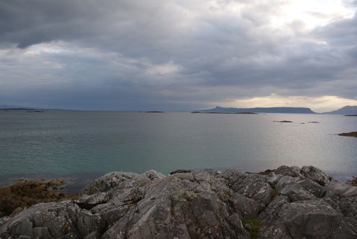 A scenic view of rocky shore and mountain landscape in Scotland under a cloudy sky