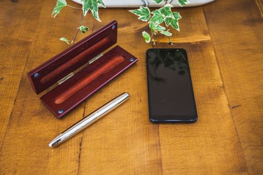 A close up shot of a mobile phone and a pen with its box on a wooden table