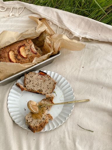 A plate of bread loaf and a spoon full of peanut butter on the beige fabric on the grass