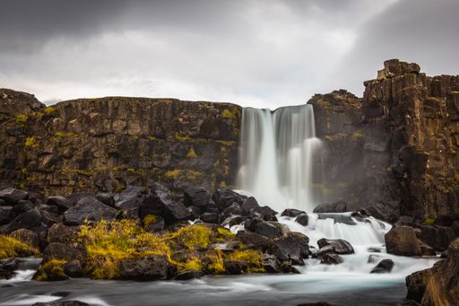 A gorgeous view of the Skogafoss waterfall in Iceland with silky water running down mossy rocks under a gloomy gray sky