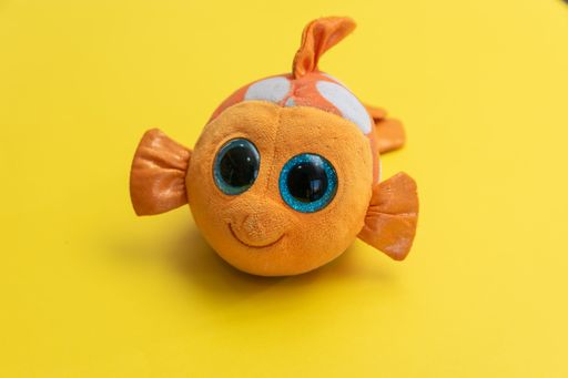 An isolated closeup shot of a clownfish plush toy in front of a yellow background