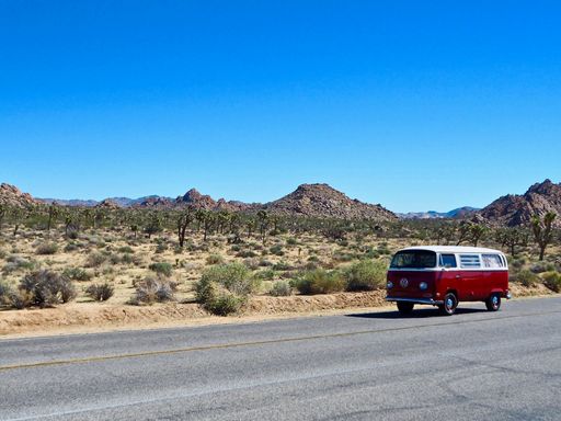 A scenic shot of a vintage red VW van driving through the Joshua Tree National Park