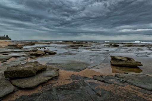 A close shot of wet rocks near the sea under a cloudy sky