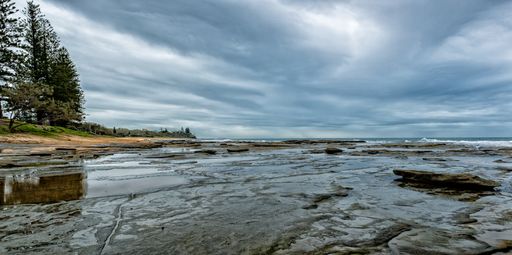 A wide shot of water in the middle of rocks near the shore under a cloudy sky in old Australia