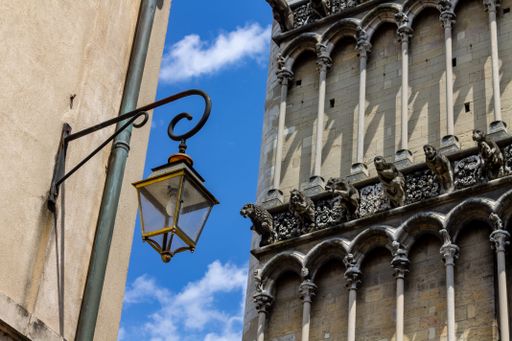 A low angle shot of an old street lantern hanging on a building by the Notre Dame de Dijon Church against blue sky on a sunny day, France