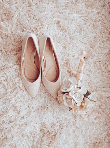 A top view of elegant bridal shoes with a beautiful bouquet on a bed