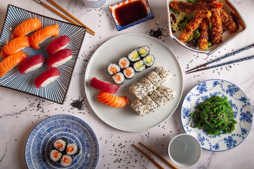 A top view of different types of sushi rolls, prawn tempura, wakame seaweed salad, soy sauce and chopsticks on a table