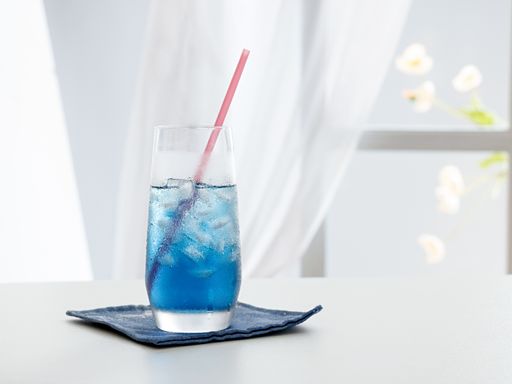 A selective focus shot of blue cocktail with ice cubes and a straw on a table near a window