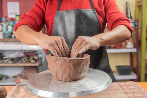 A closeup shot of Hispanic potter hands making and molding a clay vessel with both hands in his workshop