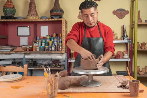 A Full length view of a Hispanic potter making a clay bowl in his workshop