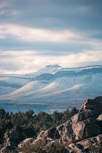 A vertical shot of rocky cliffs near snowy mountains under a cloudy gray sky in Matroosberg, South Africa