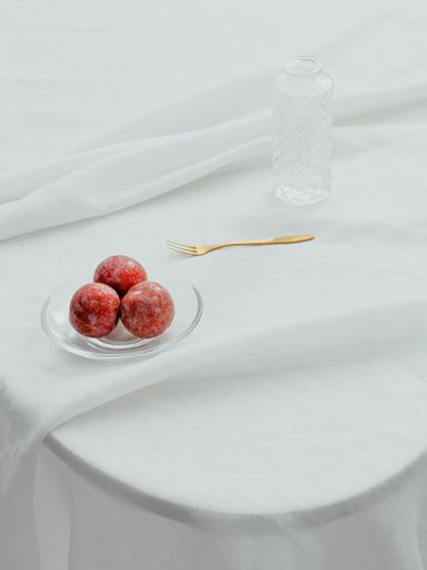A vertical aesthetic shot of apples on a transparent plate, fork and a glass bottle on a table with white fabric cover
