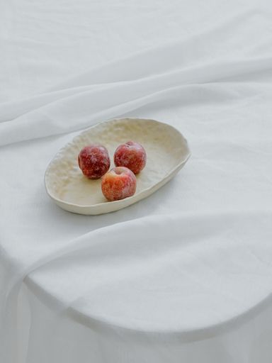 A vertical aesthetic shot of apples in a white bowl on a table with white fabric cover