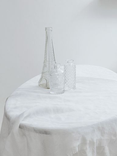 A vertical aesthetic shot of three different glass bottles on a table covered with white fabric