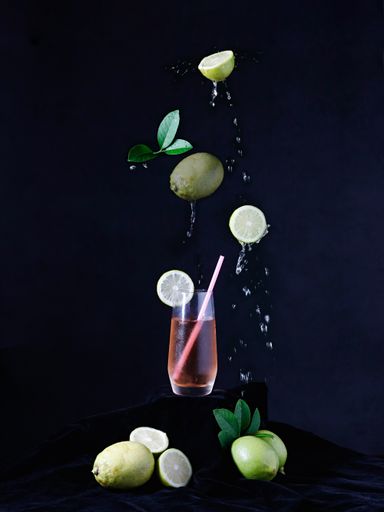 A vertical shot of a glass with lemons falling on dark surface on black background